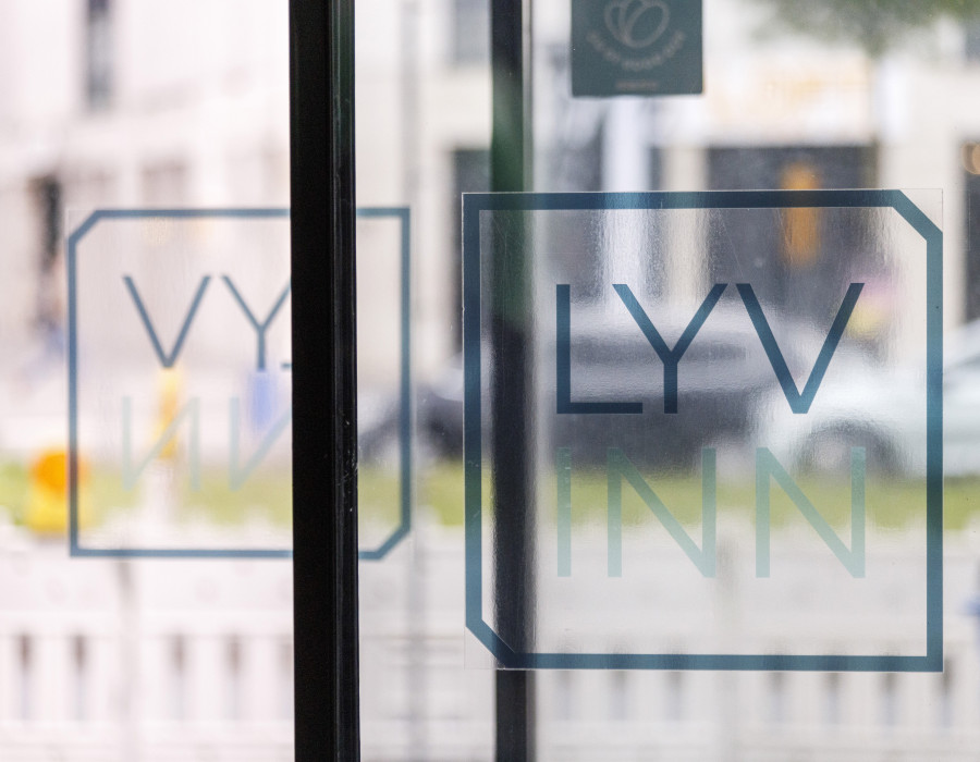 Logo „LYV INN“ auf einer Glastür von innen fotografiert mit verschwommener Straße im Hintergrund.