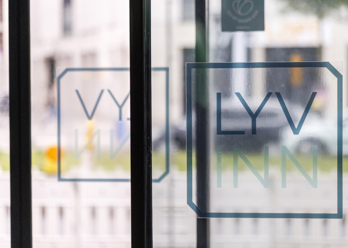Logo „LYV INN“ auf einer Glastür von innen fotografiert mit verschwommener Straße im Hintergrund.