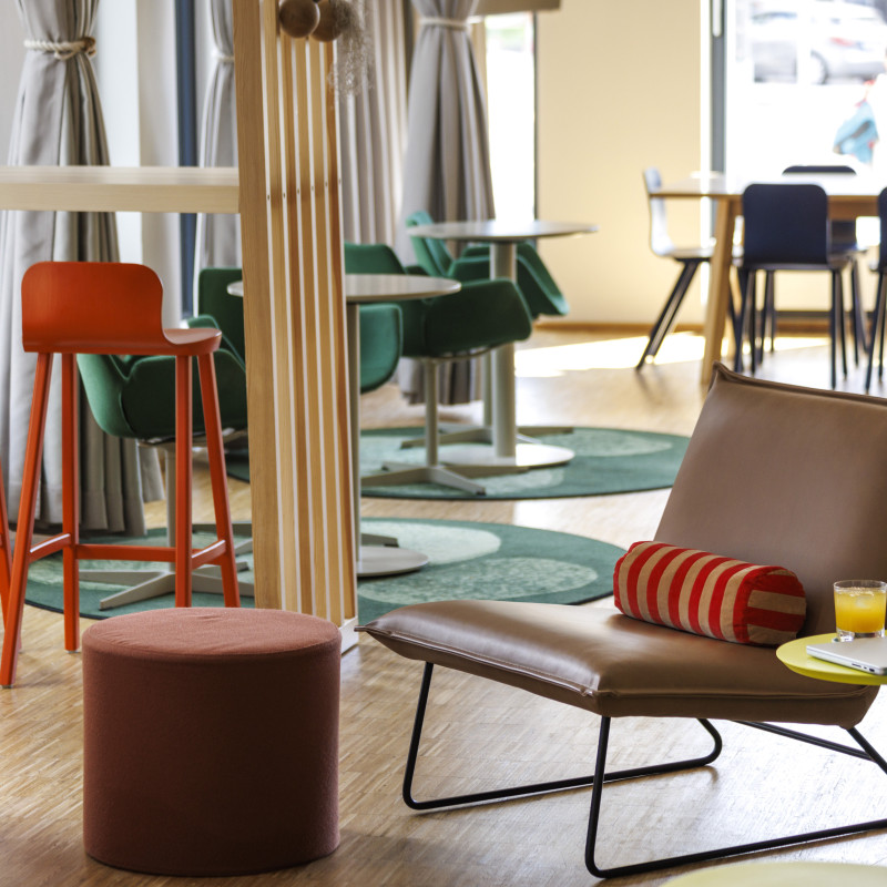 stylische Sitzecke in Hotel mit braunem Ledersessel. roten Barhockern und grünen Stühlen