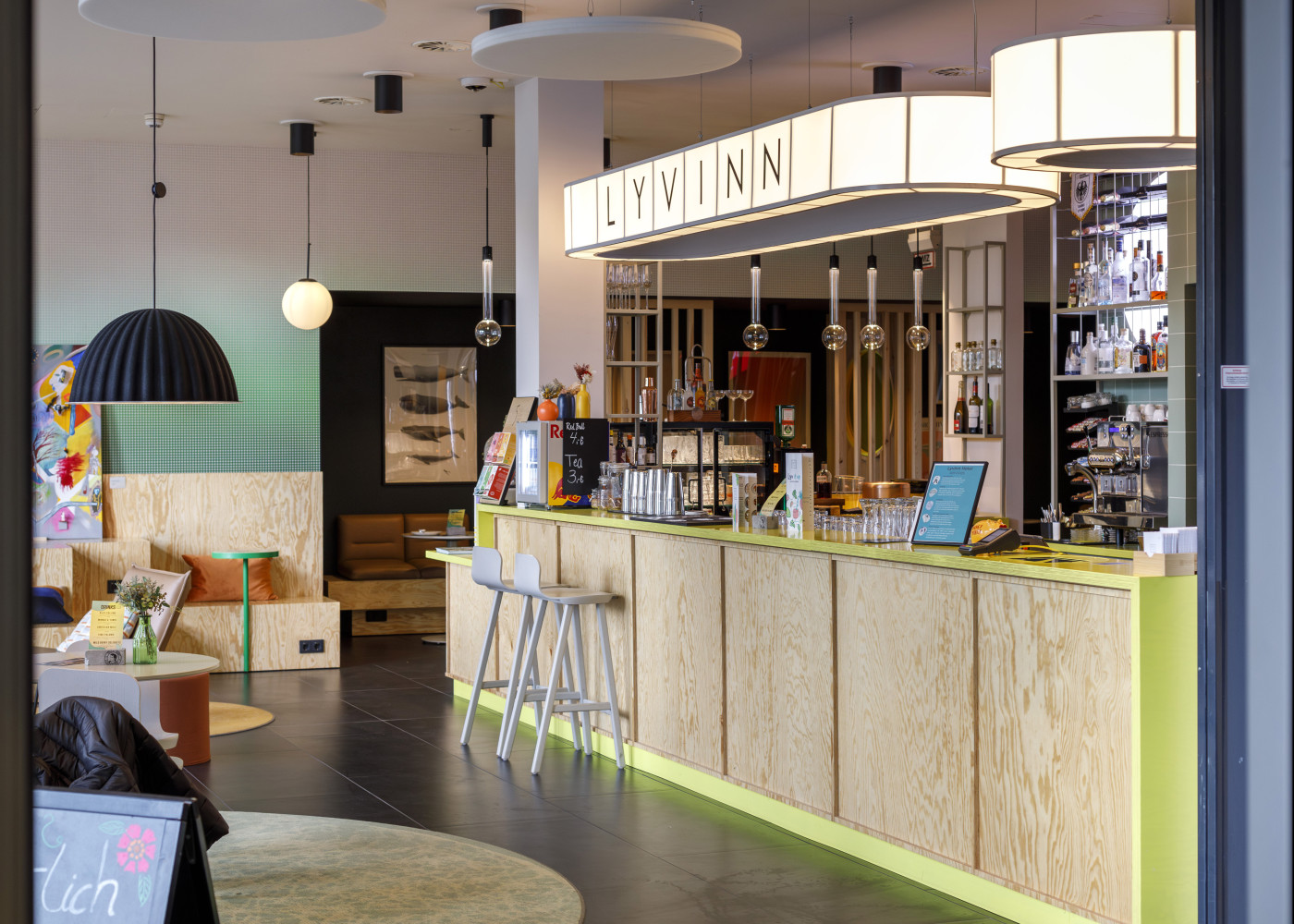 Moderne Hotelbar mit heller Theke, stilvollen Hockern und dekorativen Leuchten im offenen Lounge-Bereich.