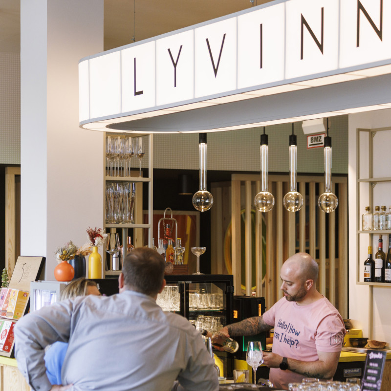 Hotelbar LYV INN mit Bartresen aus Holz, modernen Hängelampen und Gästen, die Drinks genießen.
