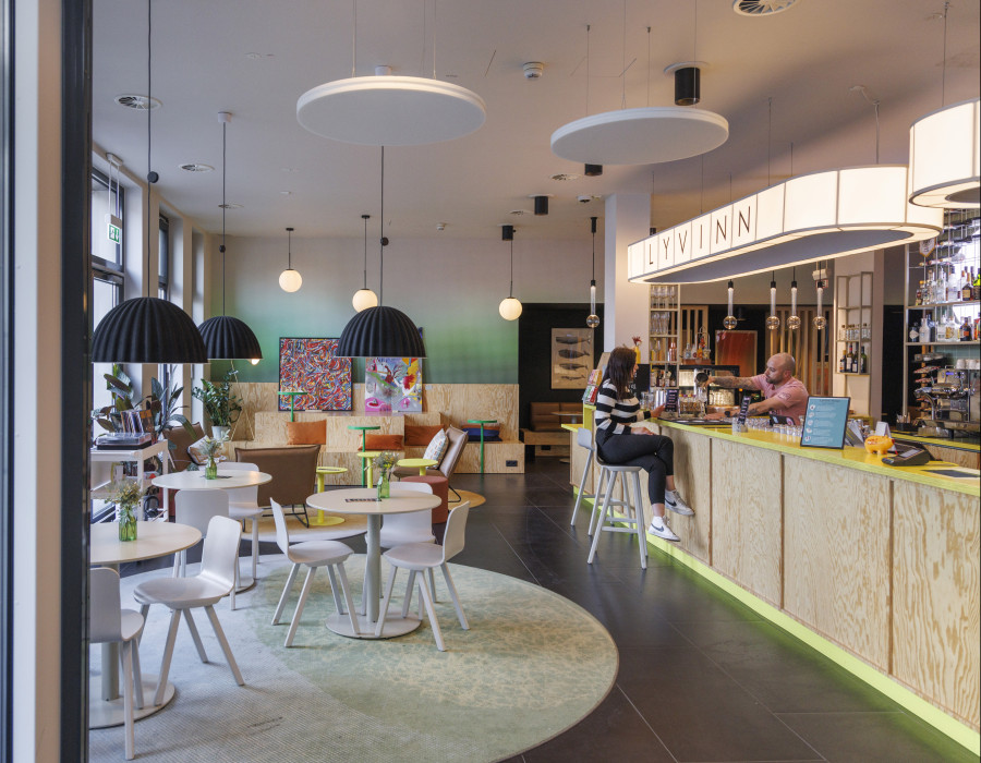 Moderner, heller Barbereich mit Gästen und Sitzgruppen, dekoriert mit Pflanzen und Designlampen.