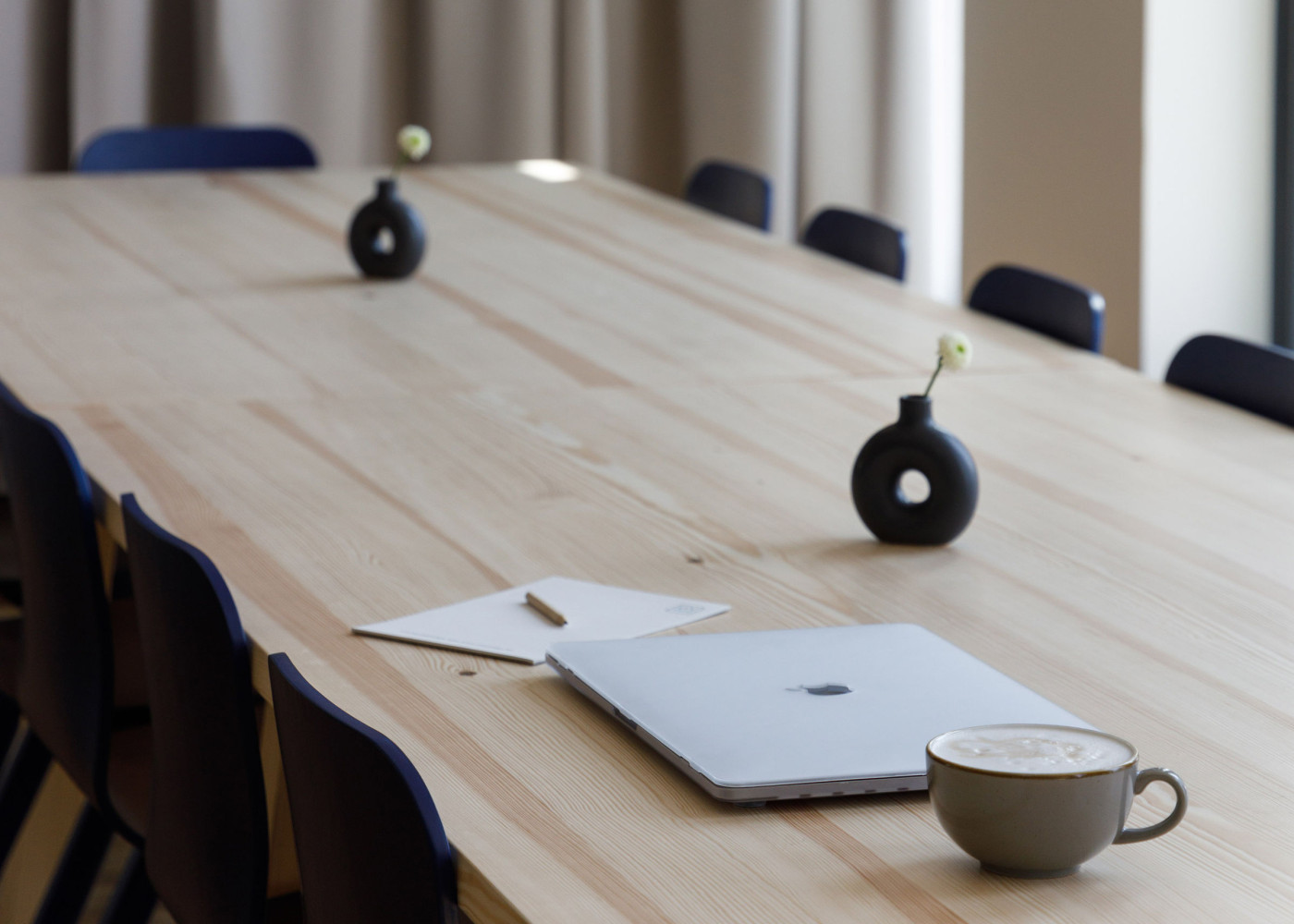 Ein Laptop, eine Kaffeetasse und ein Block liegen auf einem großen Tisch.