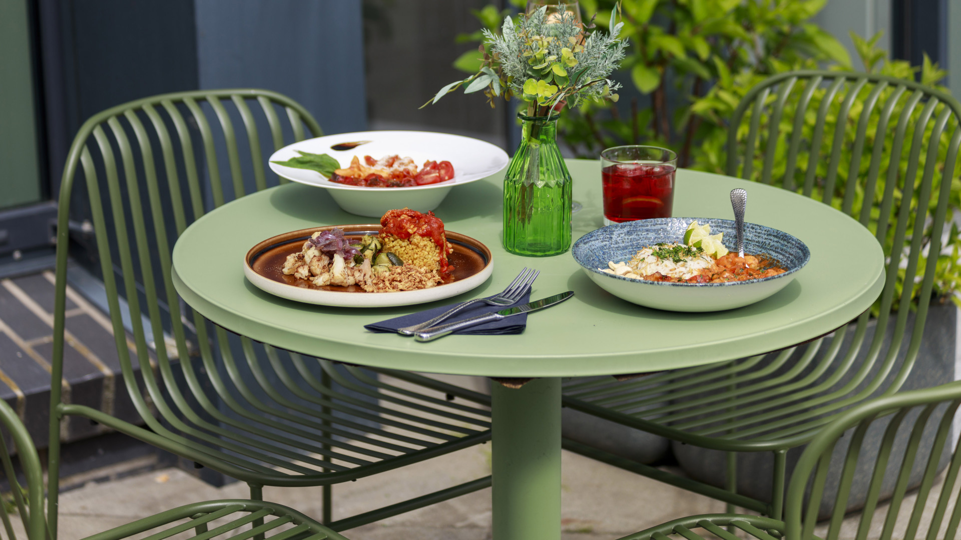 Verschiedene Gerichte auf schönen Tellern. auf einem runden, grünen Tisch im Außenbereich platziert.