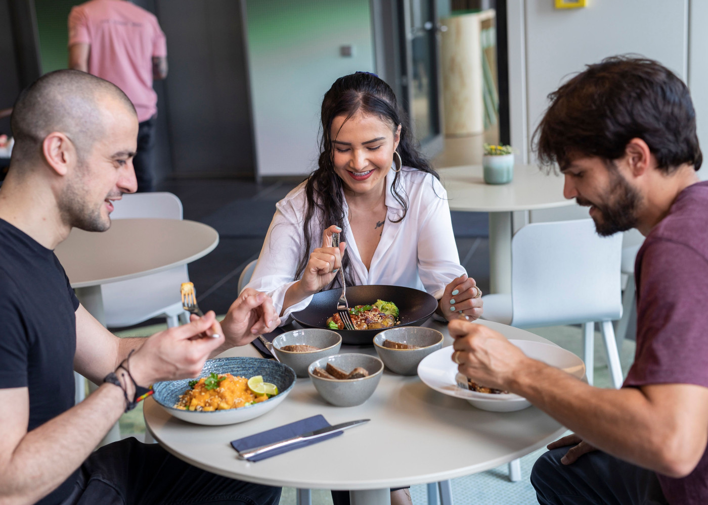 Drei Personen sitzen um einen runden Tisch und genießen ihr Essen im LyvInn Hotel.