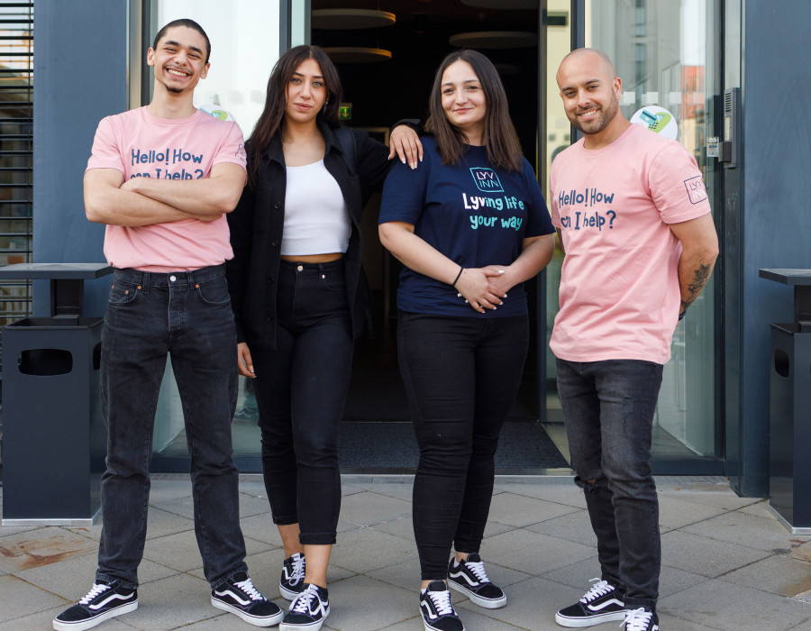 Vier Teammitglieder in legerer Kleidung stehen lächelnd vor dem Eingang des Hotels LYV INN.