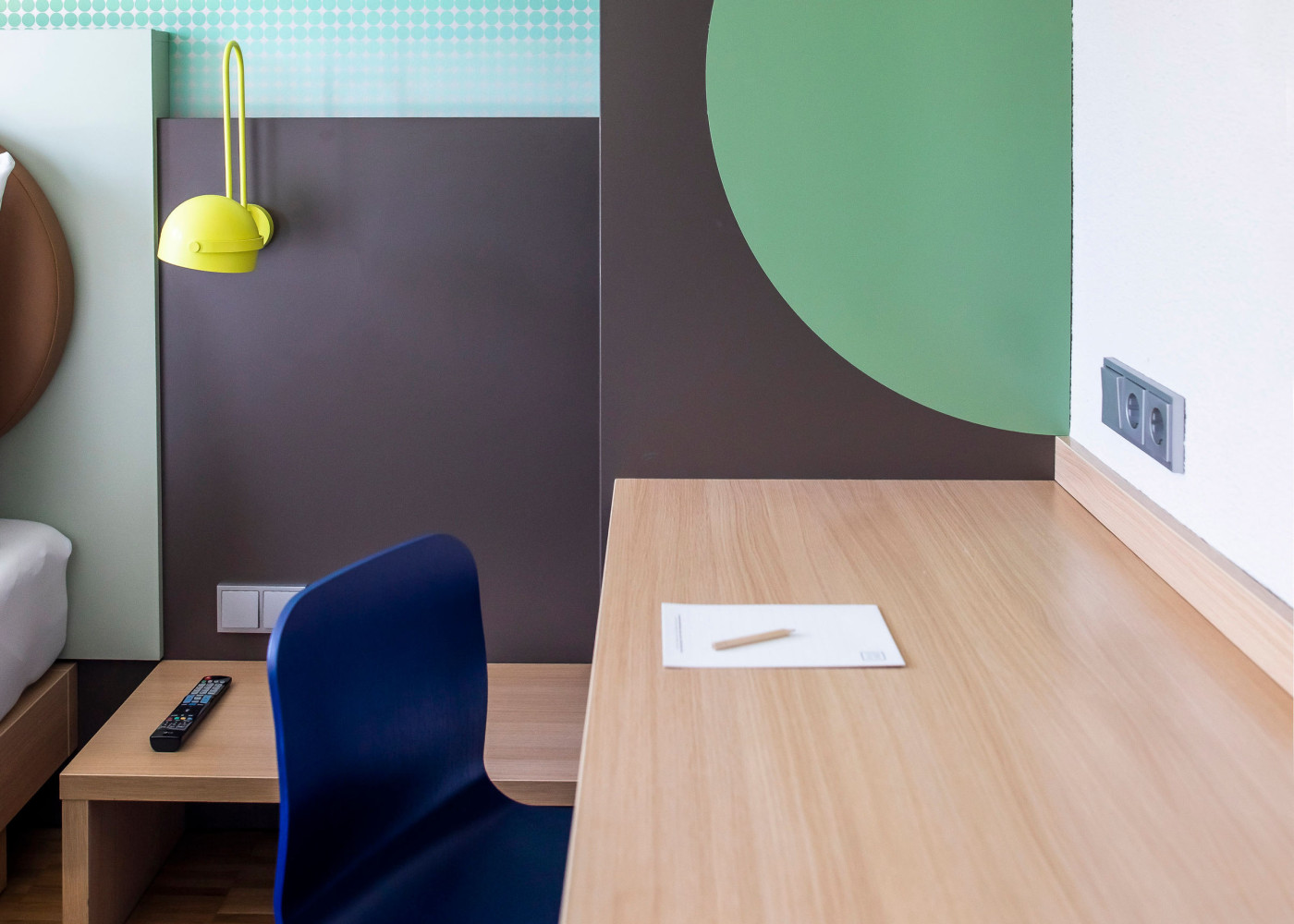 Moderner Schreibtisch mit Notizblock und farbenfroher Wandgestaltung, daneben auffällige Wandlampen.