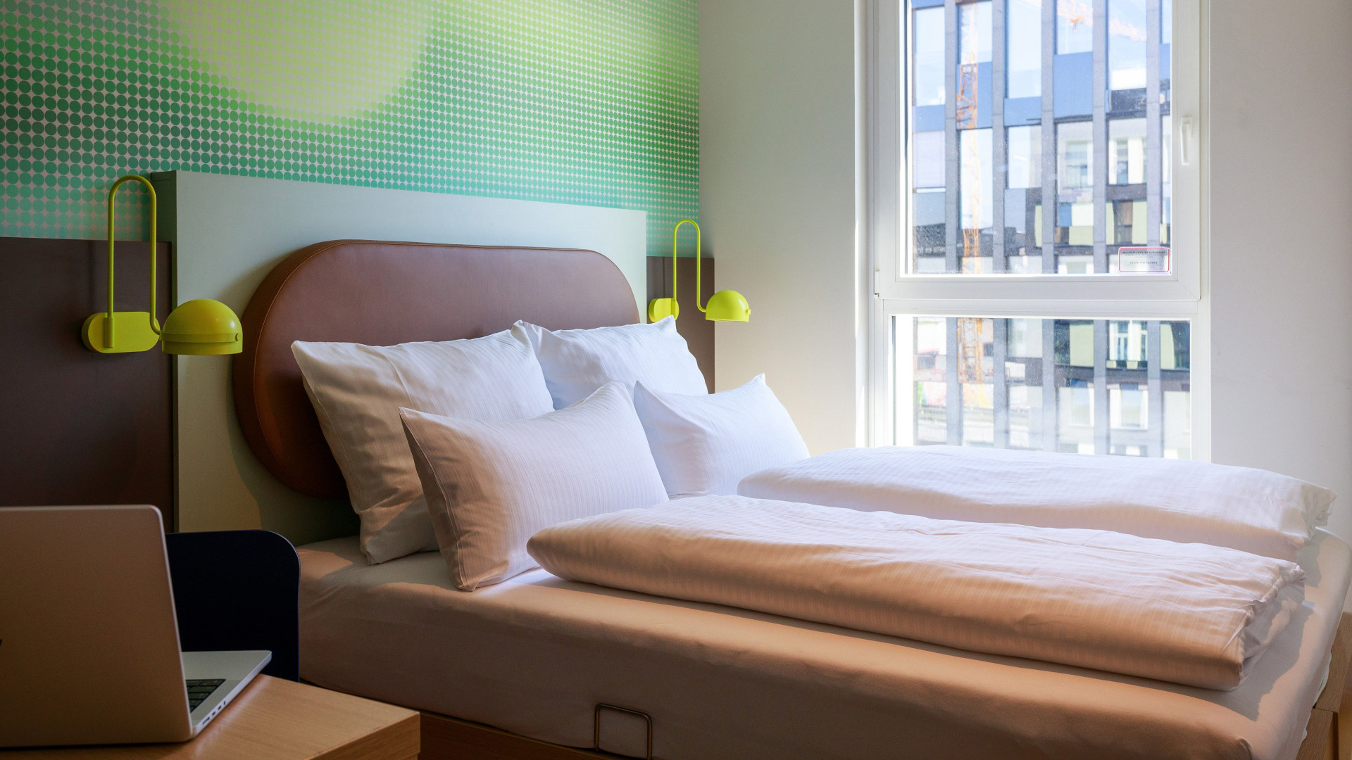 Ein frisch gemachtes Bett steht vor einem großen, hellen Fenster.