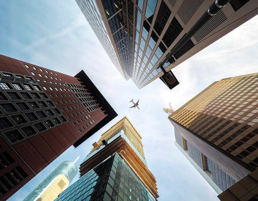 Ein Flugzeug fliegt am hellen Himmel über dicht stehenden Wolkenkratzern in einer Großstadt nach oben.